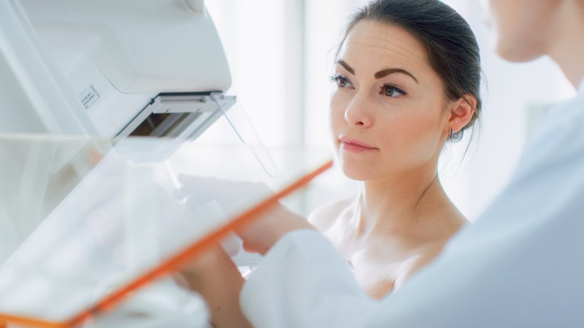 A young woman undergoing mammography screening, standing next to an imaging...